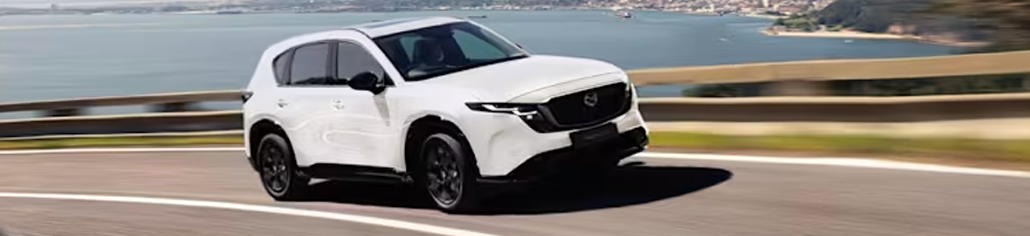 VUS Mazda blanc roulant sur une route près de l’eau